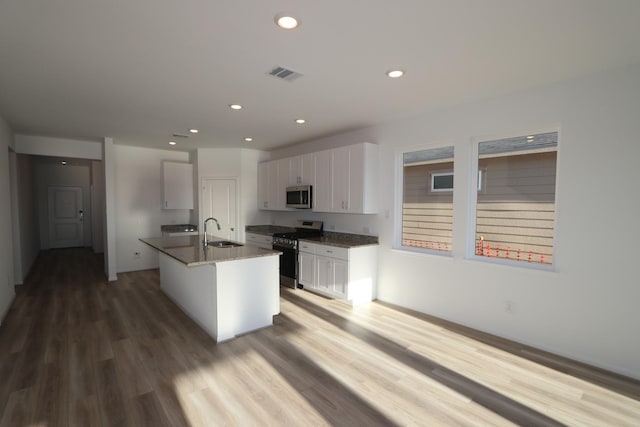 kitchen with visible vents, a kitchen island with sink, stainless steel appliances, white cabinetry, and a sink