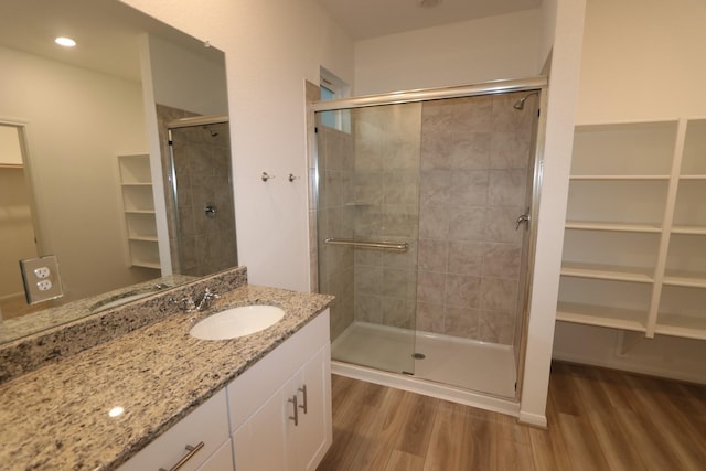 full bath featuring a stall shower, a walk in closet, vanity, and wood finished floors