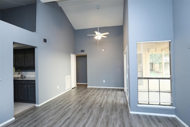 unfurnished living room with high vaulted ceiling, baseboards, visible vents, and light wood-style floors