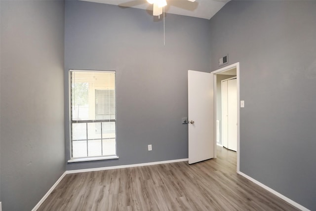 empty room with high vaulted ceiling, a ceiling fan, visible vents, baseboards, and light wood-type flooring