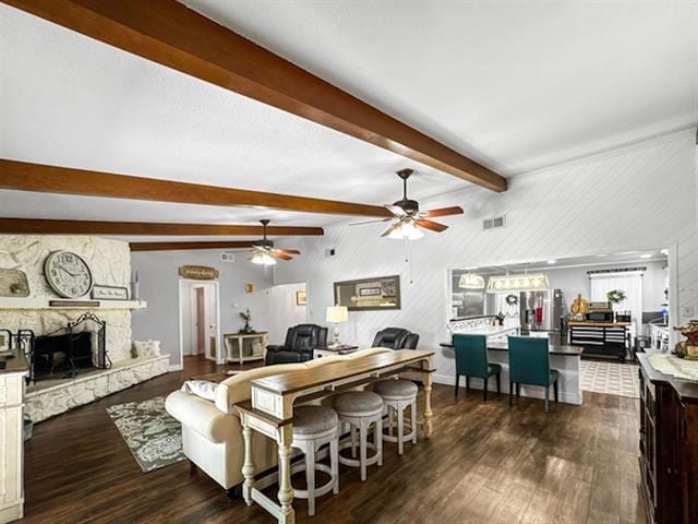 living area featuring visible vents, a ceiling fan, dark wood-type flooring, beamed ceiling, and a fireplace