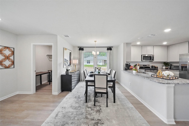 dining room with visible vents, light wood-style flooring, baseboards, and an inviting chandelier