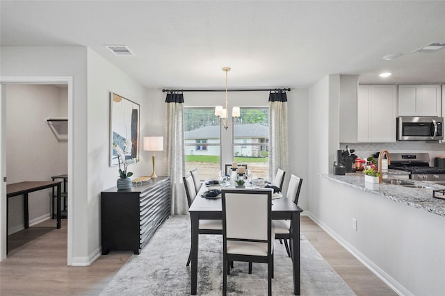 dining room with light wood-type flooring, an inviting chandelier, baseboards, and visible vents