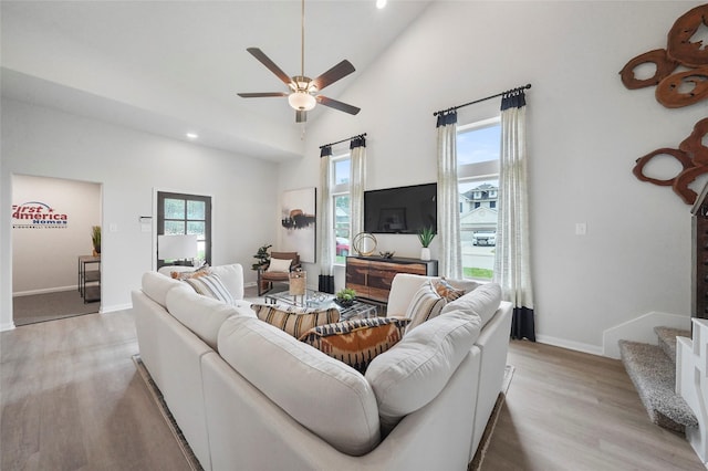 living room featuring light wood finished floors, ceiling fan, high vaulted ceiling, baseboards, and stairs