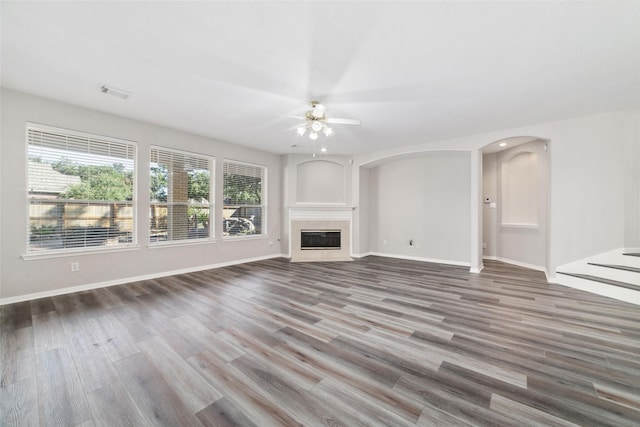 unfurnished living room with arched walkways, visible vents, a fireplace with flush hearth, ceiling fan, and wood finished floors