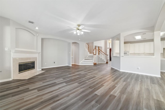 unfurnished living room featuring visible vents, arched walkways, light wood-style flooring, a premium fireplace, and stairs