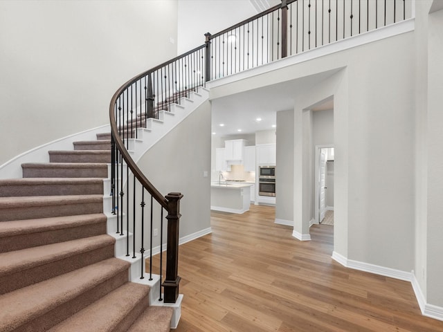 staircase featuring wood finished floors, a towering ceiling, and baseboards