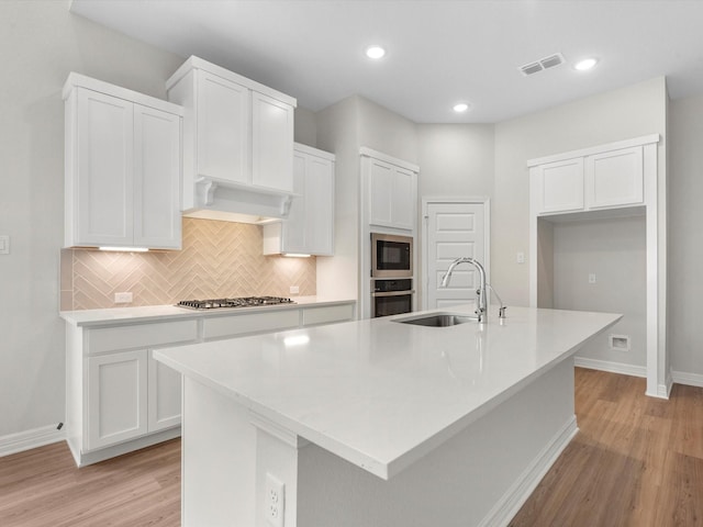 kitchen with visible vents, a kitchen island with sink, stainless steel appliances, under cabinet range hood, and a sink