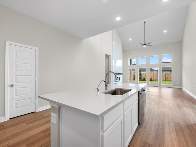 kitchen featuring a kitchen island with sink, a sink, white cabinets, open floor plan, and light countertops