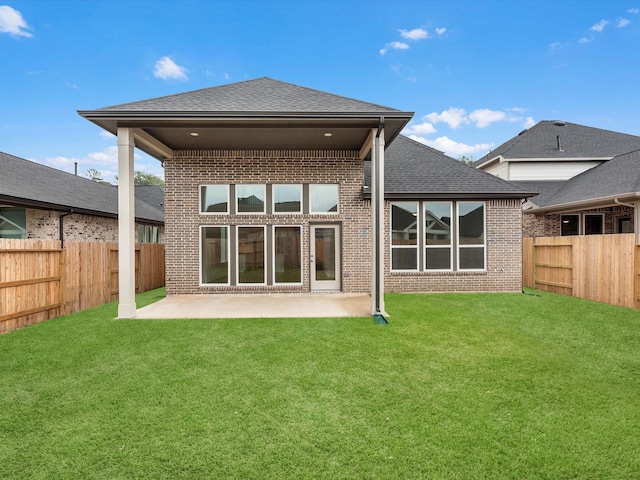 back of house featuring a fenced backyard, brick siding, a shingled roof, a lawn, and a patio area