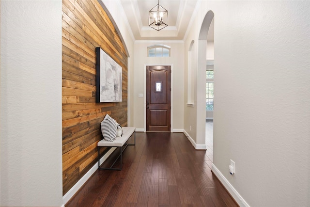 interior space with arched walkways, a notable chandelier, baseboards, ornamental molding, and dark wood-style floors