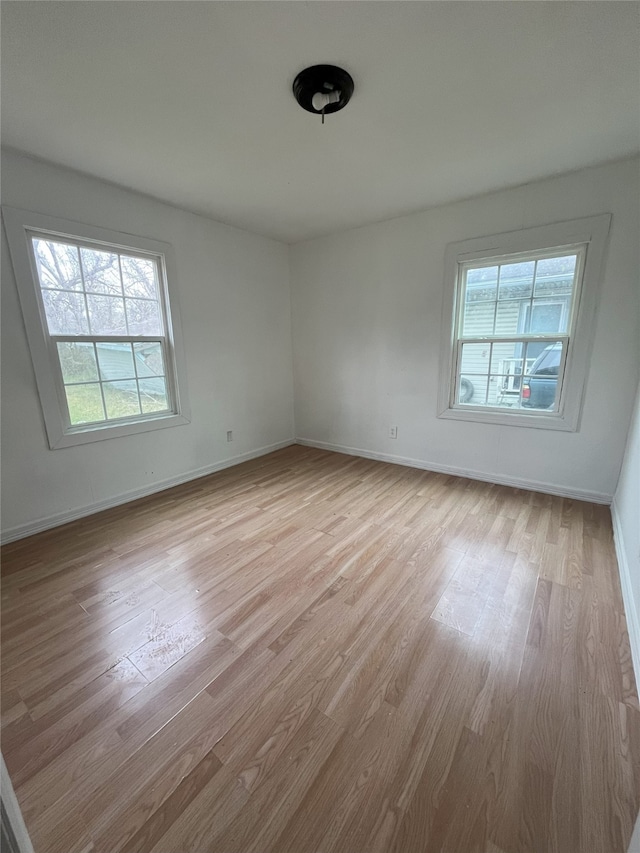 empty room featuring light wood-type flooring, plenty of natural light, and baseboards