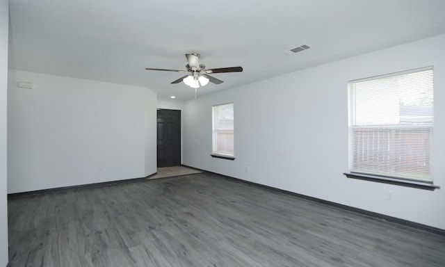 empty room featuring dark wood-style floors, ceiling fan, visible vents, and baseboards