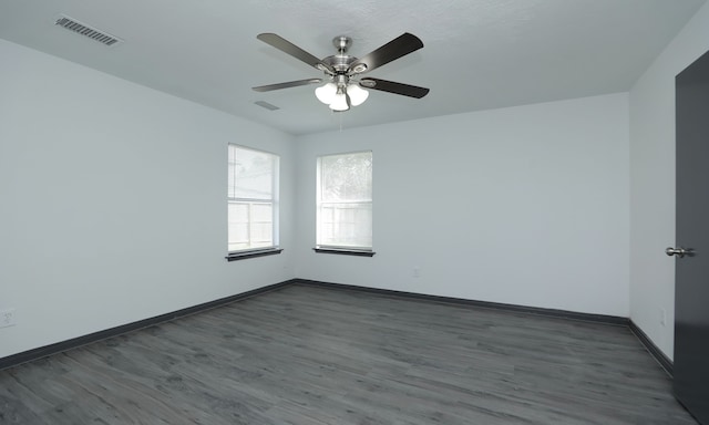 empty room featuring ceiling fan, dark wood-type flooring, visible vents, and baseboards