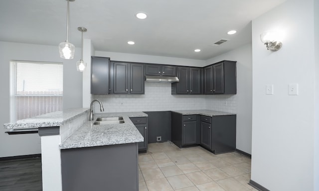 kitchen with light stone counters, pendant lighting, visible vents, a sink, and under cabinet range hood