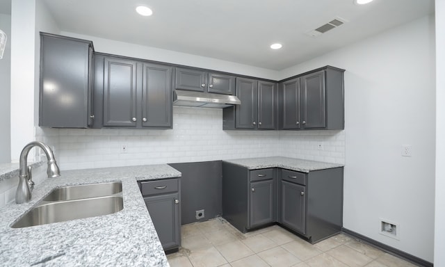 kitchen with light stone counters, under cabinet range hood, a sink, visible vents, and tasteful backsplash