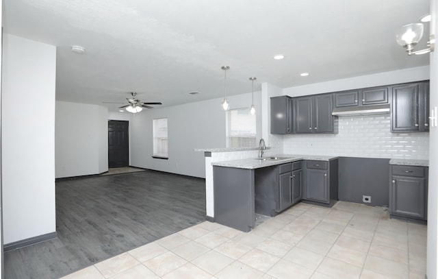 kitchen featuring open floor plan, hanging light fixtures, a peninsula, gray cabinets, and a sink