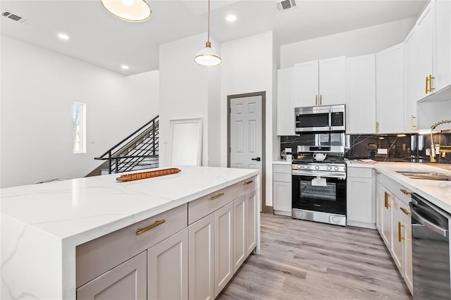 kitchen featuring appliances with stainless steel finishes, white cabinetry, visible vents, and light stone counters