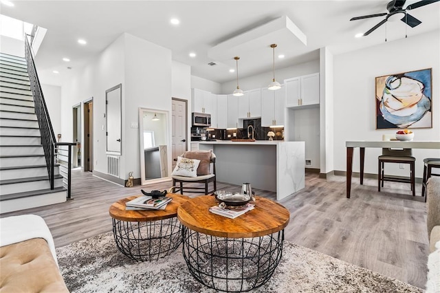 living room featuring a ceiling fan, recessed lighting, light wood finished floors, and stairs