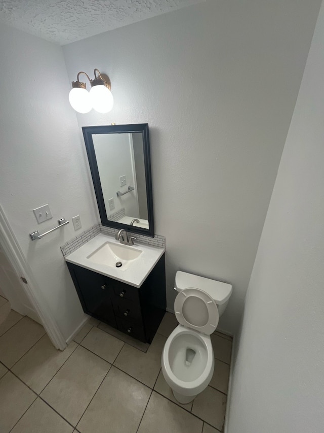 half bathroom with toilet, vanity, a textured ceiling, and tile patterned floors