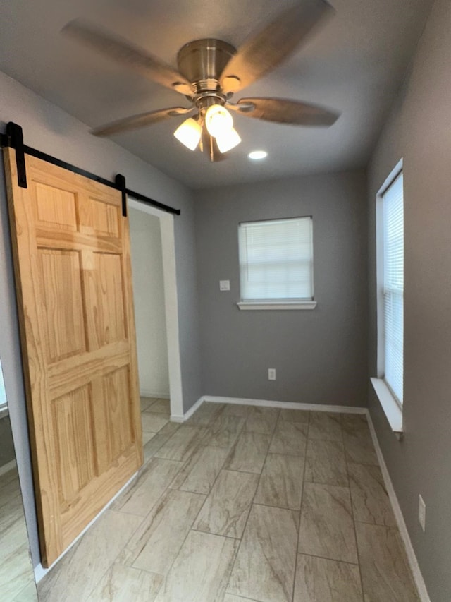 unfurnished bedroom featuring marble finish floor, a barn door, baseboards, and ceiling fan