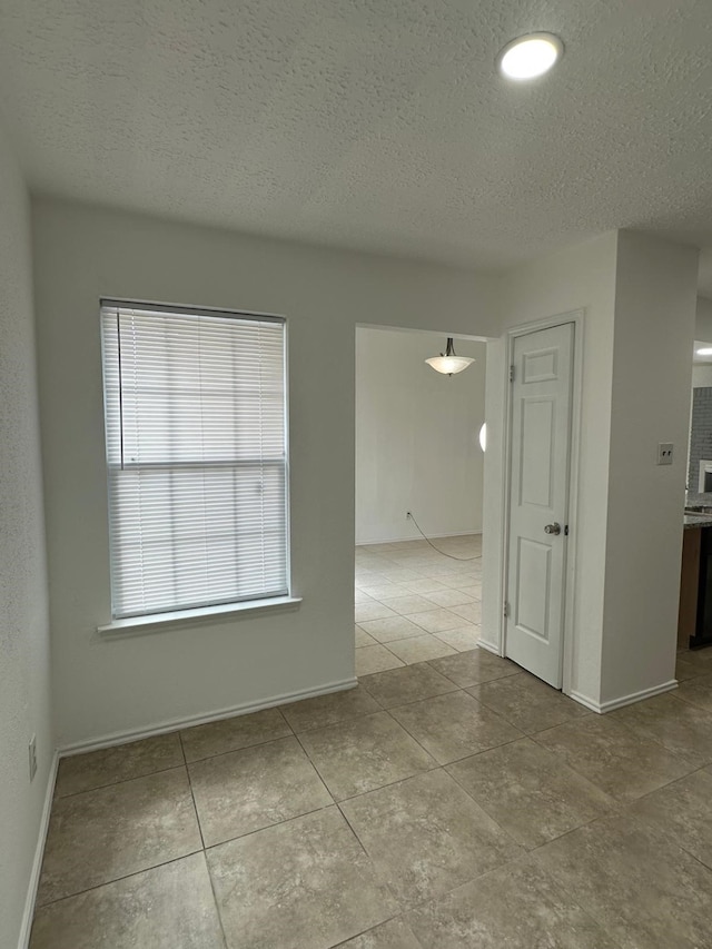 empty room featuring baseboards, a textured ceiling, and light tile patterned flooring