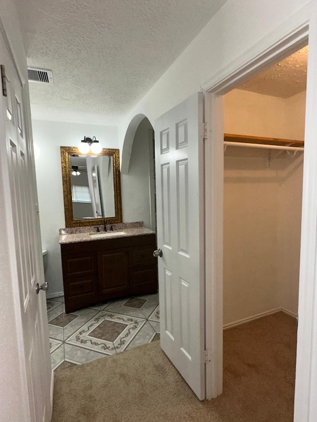 bathroom featuring visible vents, tile patterned flooring, a walk in closet, a textured ceiling, and vanity