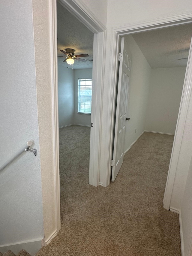 hallway featuring carpet, a textured ceiling, and baseboards