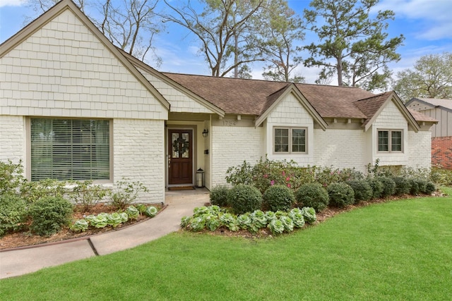 view of front facade with brick siding, a front lawn, and roof with shingles