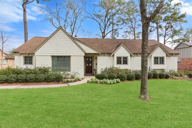 view of front facade featuring brick siding, a front yard, and a shingled roof