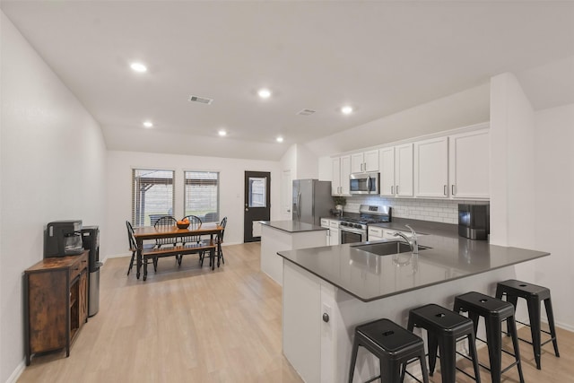 kitchen featuring dark countertops, a kitchen breakfast bar, a peninsula, stainless steel appliances, and white cabinetry