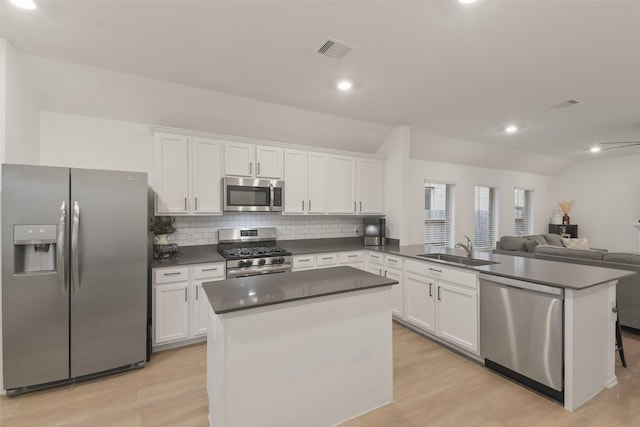 kitchen featuring white cabinets, dark countertops, appliances with stainless steel finishes, a peninsula, and a sink