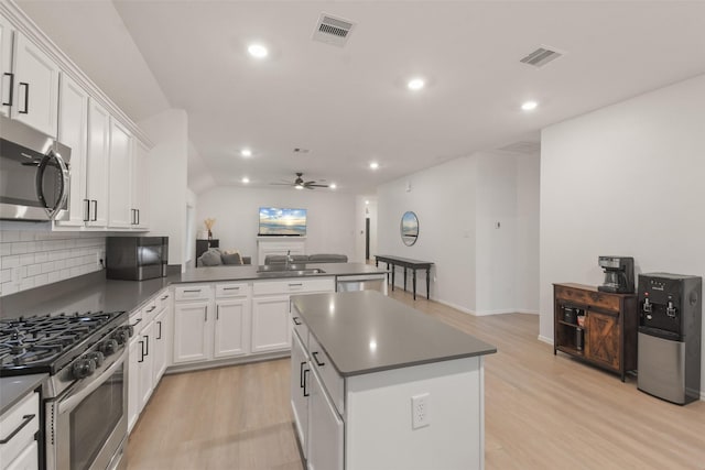 kitchen featuring open floor plan, stainless steel appliances, dark countertops, and white cabinetry