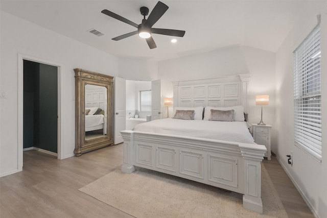 bedroom featuring light wood finished floors, baseboards, visible vents, ensuite bath, and ceiling fan