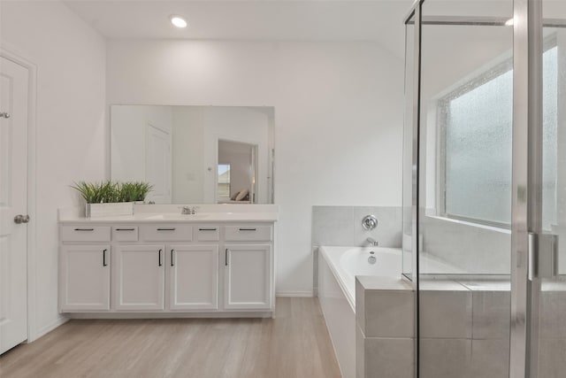 bathroom featuring wood finished floors, a stall shower, a garden tub, and vanity