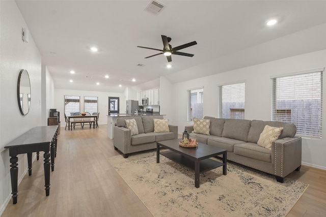 living room featuring a healthy amount of sunlight, visible vents, vaulted ceiling, and light wood-style flooring