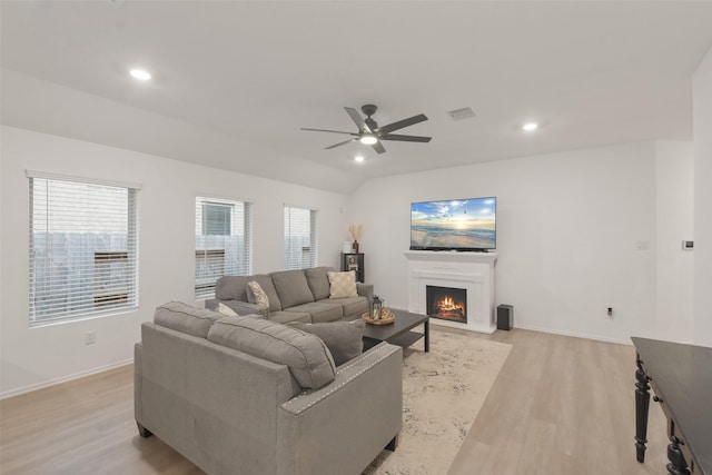 living area with light wood-type flooring, a warm lit fireplace, baseboards, and lofted ceiling