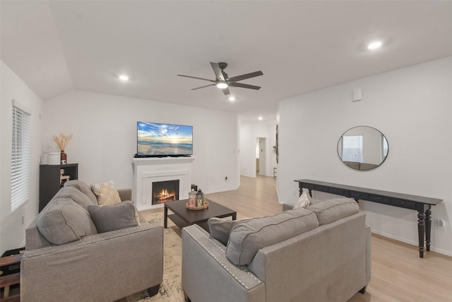 living room with lofted ceiling, a fireplace with flush hearth, a ceiling fan, and light wood-style floors