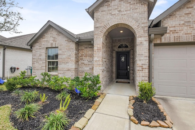 entrance to property featuring an attached garage, roof with shingles, and brick siding