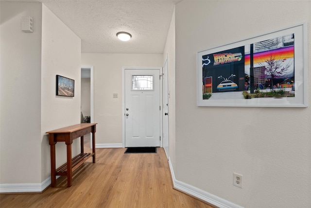 foyer entrance with light wood-style flooring, baseboards, and a textured ceiling