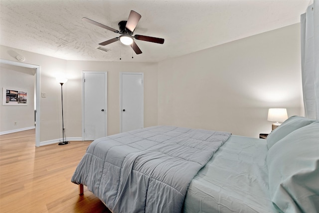 bedroom featuring baseboards, visible vents, ceiling fan, wood finished floors, and a textured ceiling