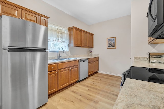 kitchen with appliances with stainless steel finishes, a sink, light wood-style floors, light countertops, and brown cabinetry