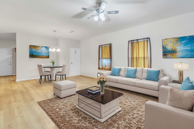 living room featuring baseboards, light wood-style flooring, and ceiling fan with notable chandelier