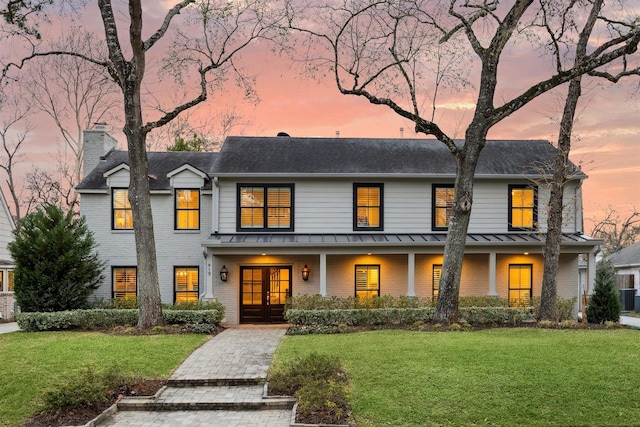 view of front of home with a standing seam roof, brick siding, a lawn, and french doors