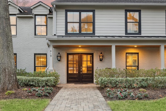 view of exterior entry with french doors, brick siding, metal roof, and a standing seam roof