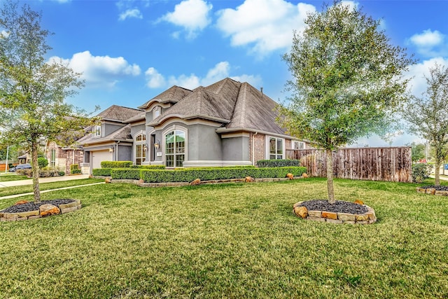 view of front facade featuring an attached garage, brick siding, fence, stucco siding, and a front lawn