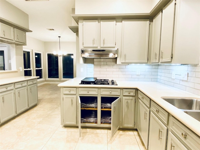 kitchen with hanging light fixtures, under cabinet range hood, gas cooktop, and light countertops