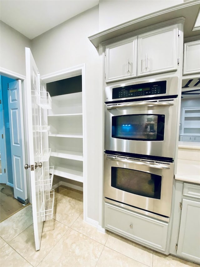 kitchen with light tile patterned floors, double oven, light countertops, and white cabinetry