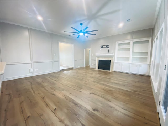 unfurnished living room with visible vents, a ceiling fan, wood finished floors, a fireplace, and a decorative wall