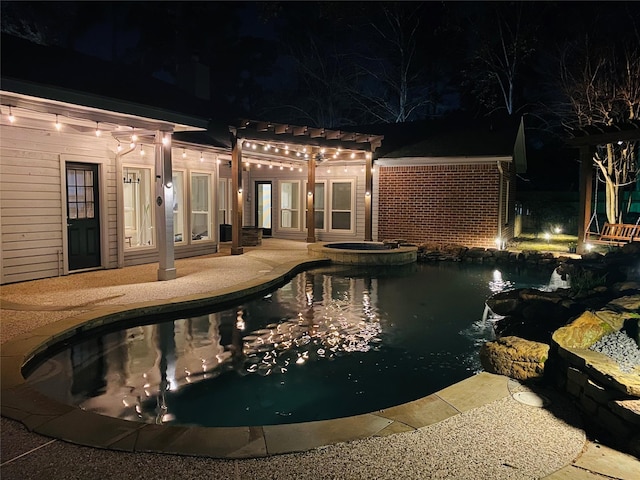 pool at night with a patio area and a pool with connected hot tub